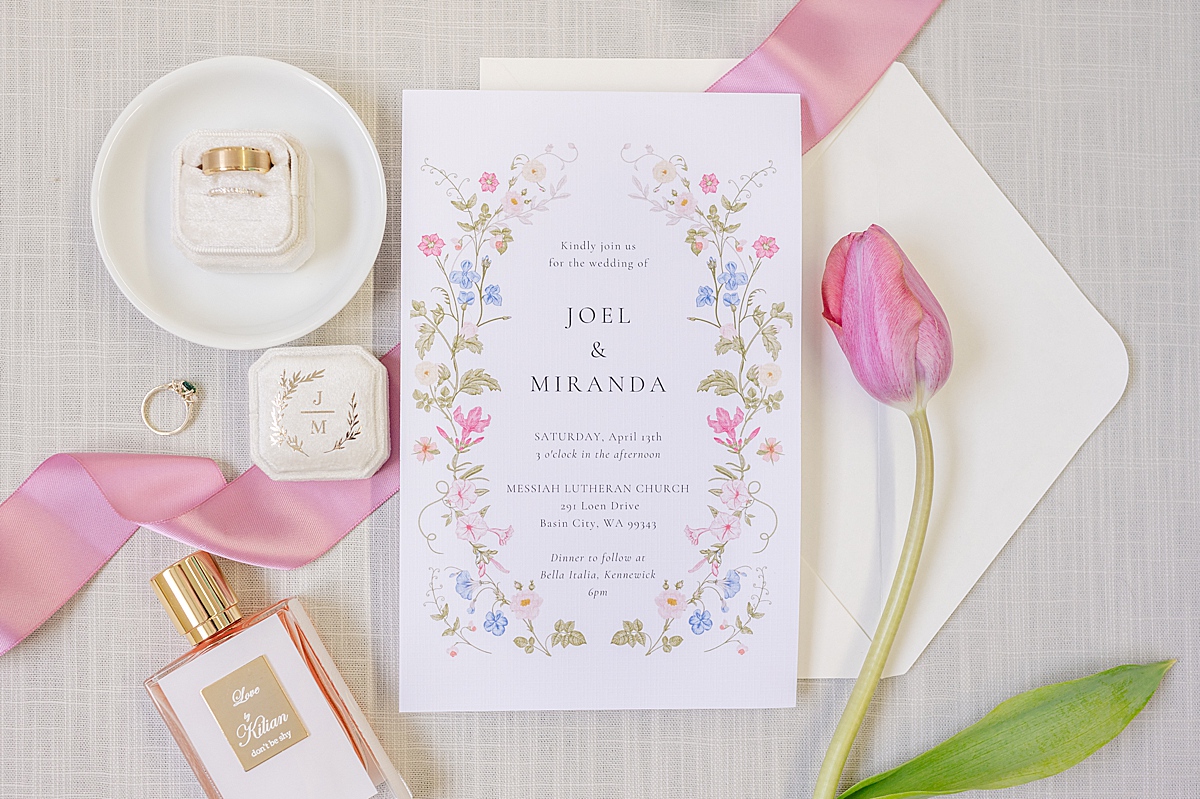 Wedding invitation, rings, perfume bottle and pink tulip arranged beautifully on a neutral background